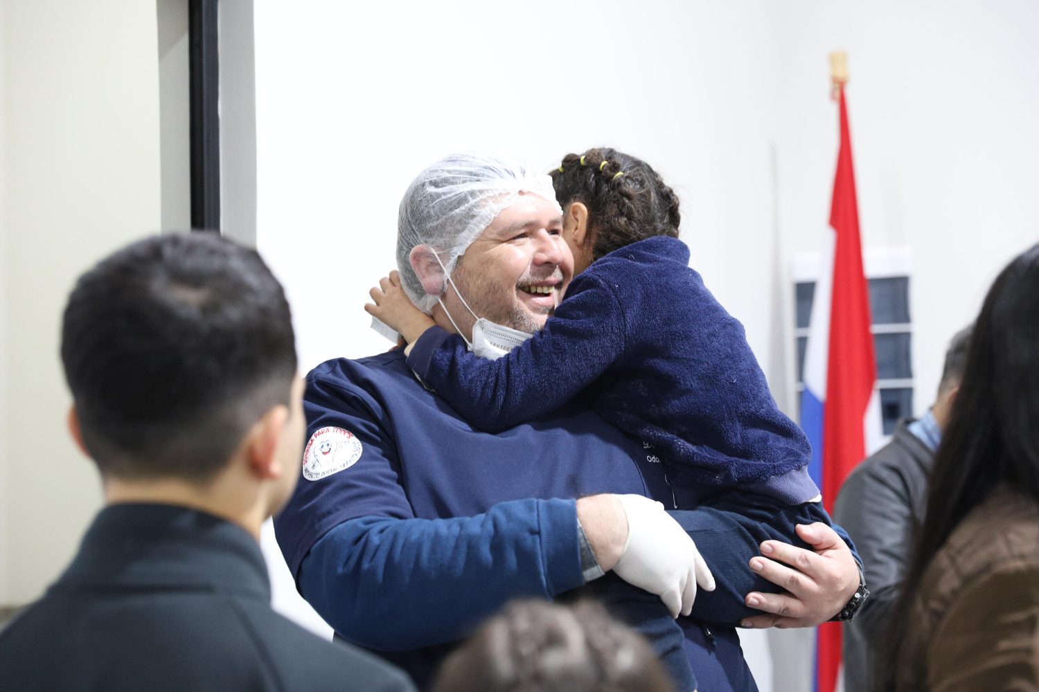 Odontólogo abrazando a una niña, con la bandera de Paraguay